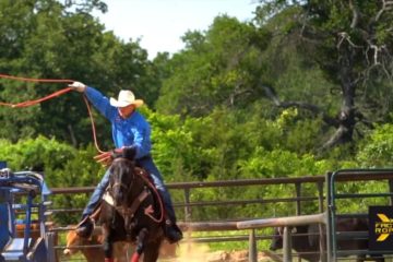 Image of man wearing cowboy hat roping from the back of a horse.